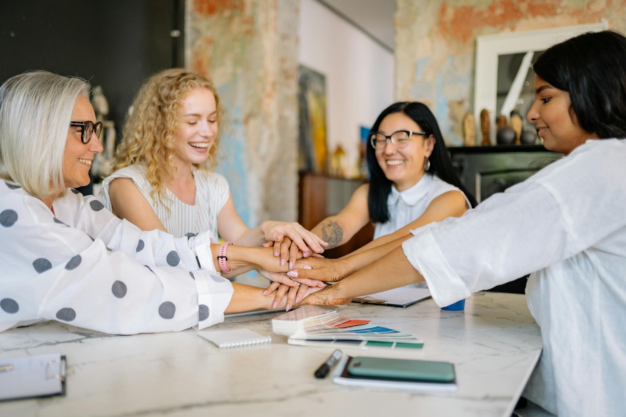 Diverse group of businesswomen collaborating at a desk, embracing teamwork with smiles and positivity.