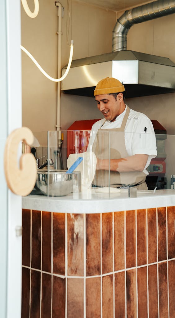 Chef in a modern kitchen preparing food with a smile, showcasing culinary skills.