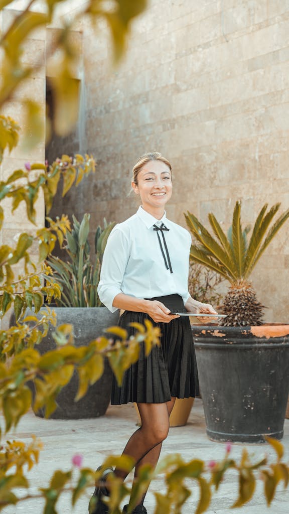 Young woman in black skirt smiling with digital tablet in outdoor garden setting.